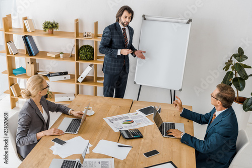 young businessman standing near board and speaking at meeting in office