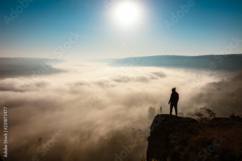 Black silhouette of a man standing on a rock over a foggy valley