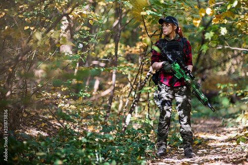 Woman bodyguard stands among the bushes/Young woman stands with a rifle in the hands among the bushes in the forest