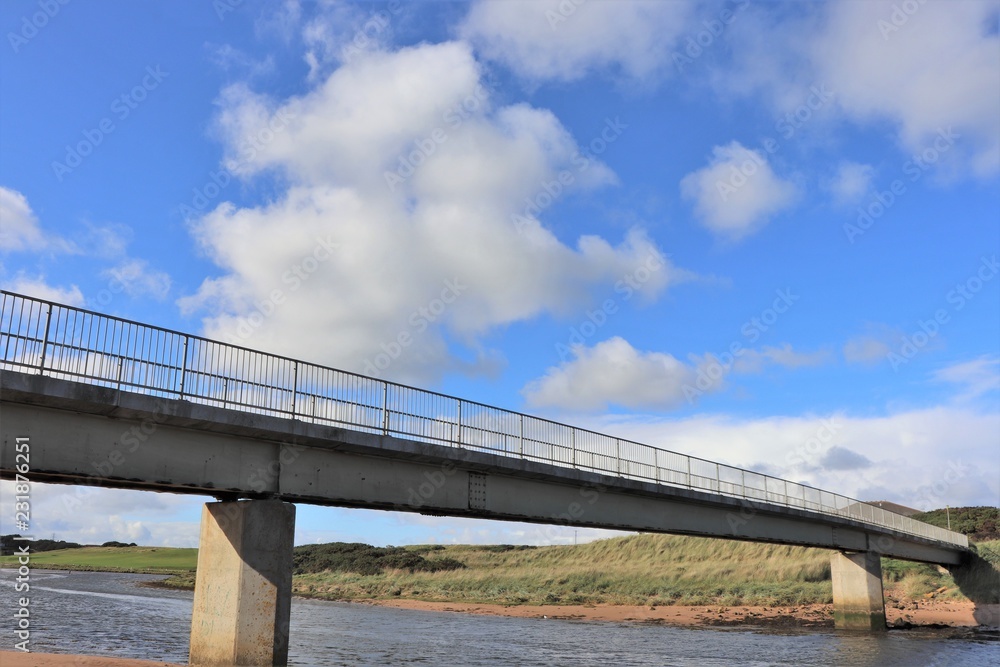 Bridge over river with fluffy white clouds and blue sky