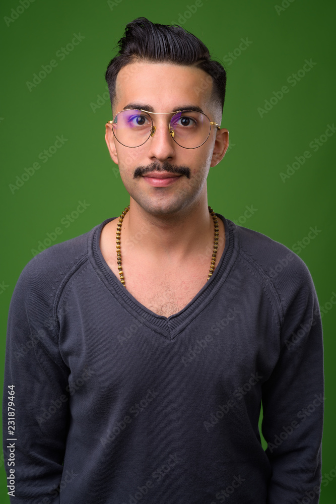 Young handsome Iranian man with mustache against green backgroun