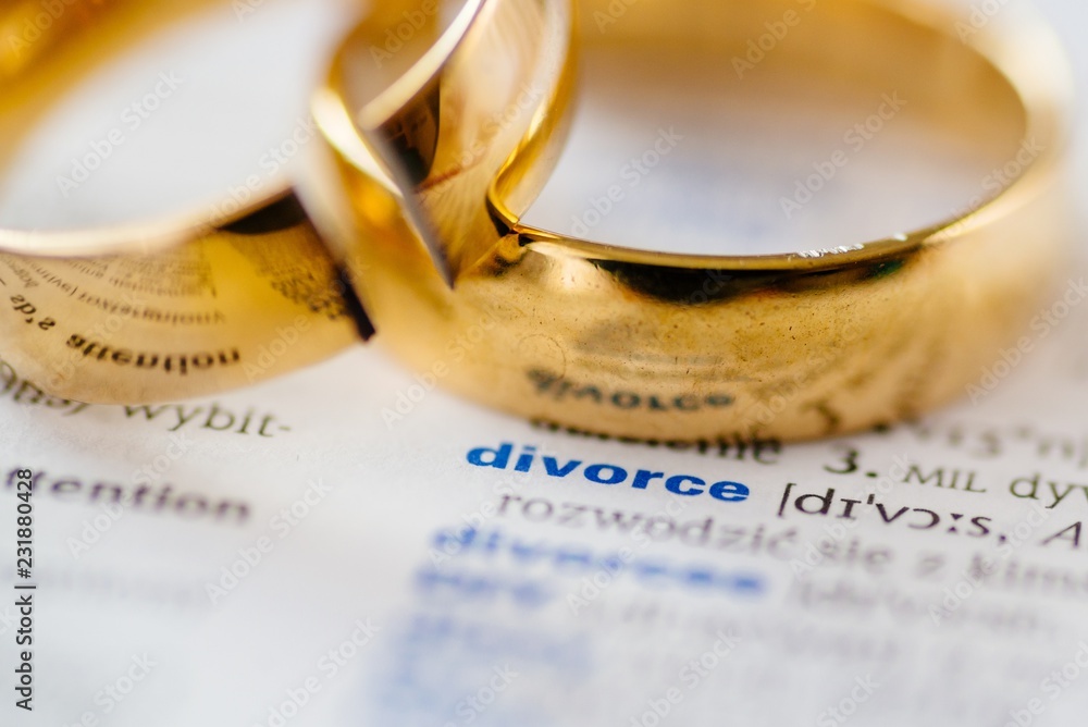 Two broken wedding rings on divorce word in dictionary.