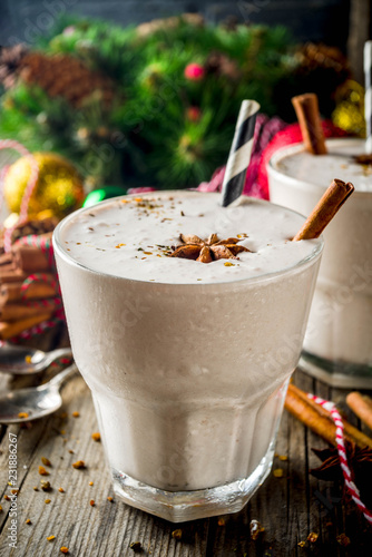 Christmas sweet cold drink, Homemade eggnog milkshake in two glasses with cinnamon and anise, old wooden background with xmas decorations copy space
