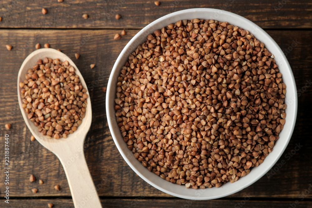 Dry buckwheat groats in a white bowl with a spoon on a wooden brown table. cereals. healthy food. porridge. top view Dry buckwheat groats in a white bowl with a spoon on a wooden brown table. cereals. healthy food. porridge. top view