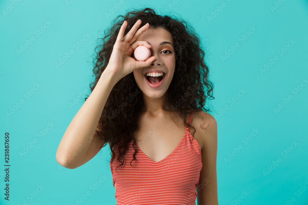Photo of caucasian woman 20s with curly hair smiling and eating macaron biscuit, isolated over blue background Photo of caucasian woman 20s with curly hair smiling and eating macaron biscuit, isolated over blue background