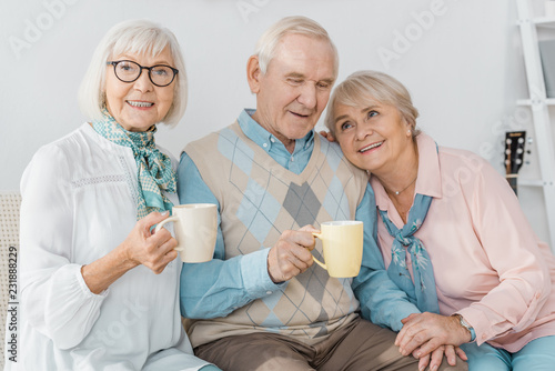happy senior people sitting on sofa and drinking tea together