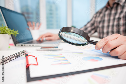 Businessman analyzing business graphs with magnifying glass