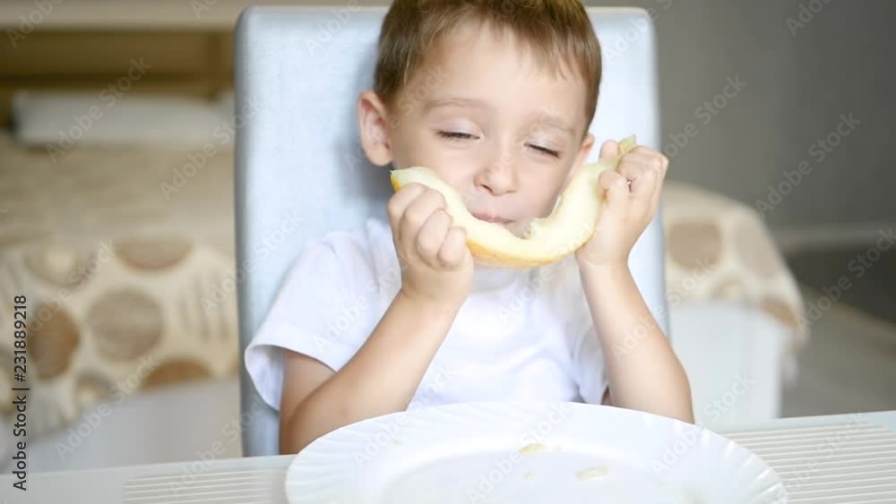 A child eats a melon while sitting at a table in slow motion. A child eats a melon while sitting at a table in slow motion.
