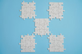 Fragment of a folded white jigsaw puzzle and a pile of uncombed puzzle elements against the background of a blue surface.