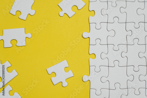 Fragment of a folded white jigsaw puzzle and a pile of uncombed puzzle elements against the background of a yellow surface.