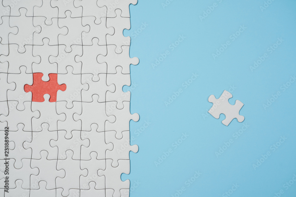 Fragment of a folded white jigsaw puzzle and a pile of uncombed puzzle elements against the background of a blue surface.