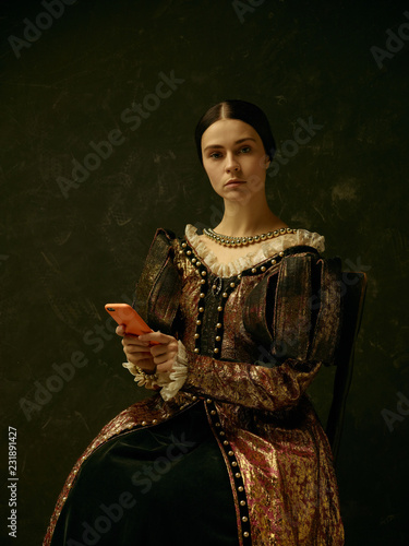 Portrait of a girl wearing a princess or countess dress with mobile phone over dark studio