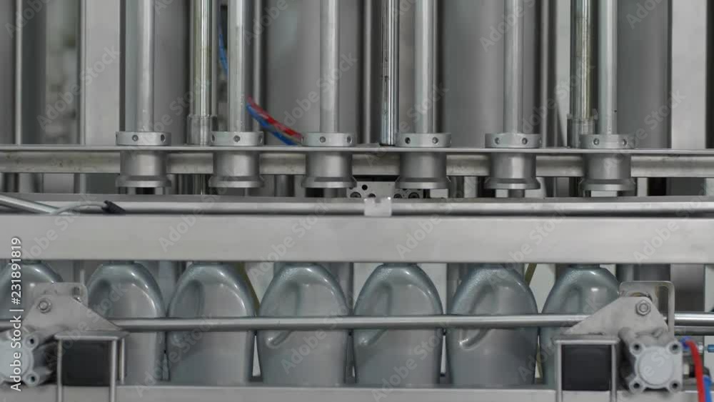 industrial equipment filling engine oil in to the gray plastic bottles on a moving conveyor line at factory industrial equipment filling engine oil in to the gray plastic bottles on a moving conveyor line at factory