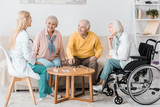 young female nurse playing domino with senior patients