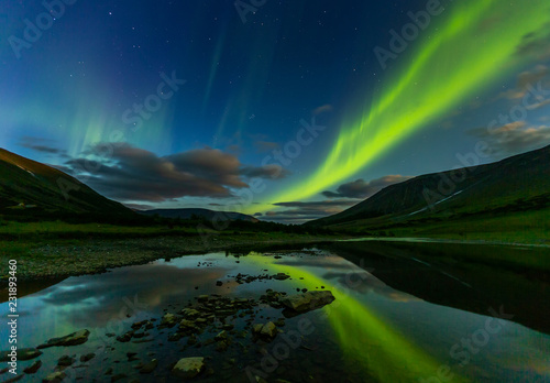 aurora borealis in the night sky cut the mountains, reflected in the water.