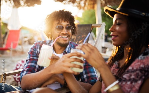 Young happy black couple with drinks relaxing on the beach