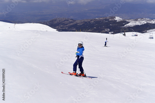 A boy in ski suit, helmet and sunglasses skiing from snowy mountains in Serra Nevada