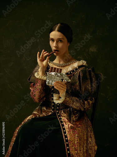 Portrait of a girl wearing a princess or countess dress over dark studio. portrait with sweet chocolate bar over dark studio