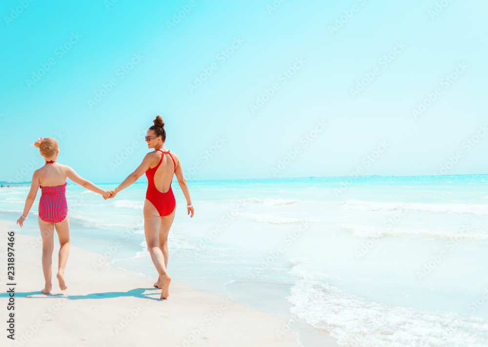 Fototapeta premium young mother and child in red beachwear on seacoast walking