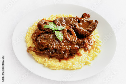 beef shank braised with wine and vegetables, garnished with risotto, and decorated with basil