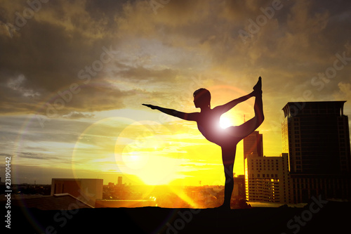 Silhouette of woman practicing yoga on the building at sunset