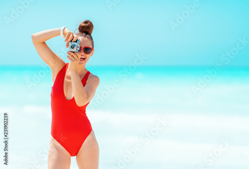 smiling woman taking photos with retro photo camera on seashore