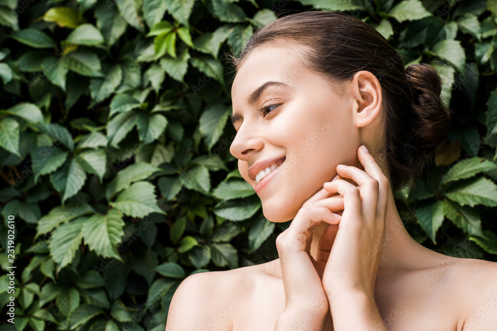 smiling young woman with hands near face on green leaves background smiling young woman with hands near face on green leaves background
