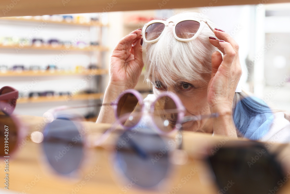 Okulary przeciwsłoneczne. Salon optyczny.  Starsza kobieta kupuje okulary przeciwsłoneczne - obrazy, fototapety, plakaty 