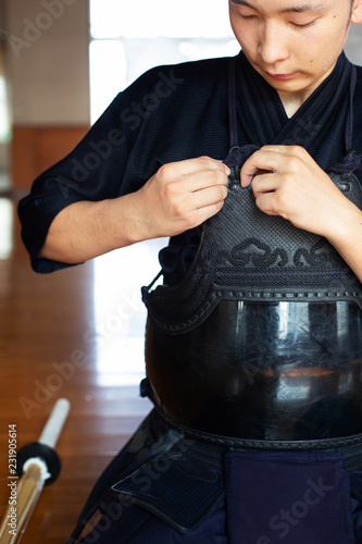 Male Japanese Kendo fighter kneeling on floor, fastening his breastplate. photo
