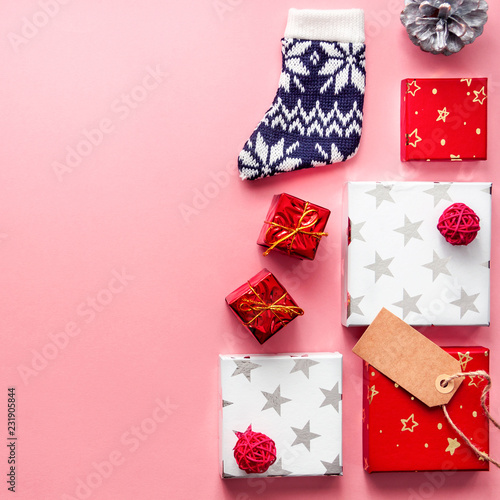 Square photo of a pink pastel Christmas card with copy space, red and white presents with stars, red balls, pine cone and woolen sock