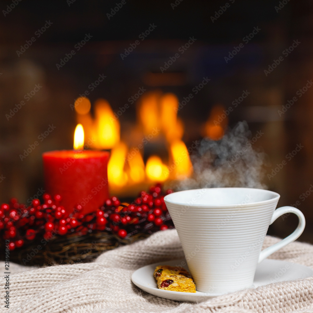 Cup of hot drink with steam and cookie berries red candle in Christmas decoration on knitted plaid in front of fireplace. Christmas New Year concept. Cozy relaxed magical atmosphere home interior. Cup of hot drink with steam and cookie berries red candle in Christmas decoration on knitted plaid in front of fireplace. Christmas New Year concept. Cozy relaxed magical atmosphere home interior.