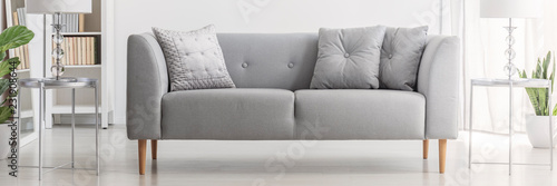Light grey sofa with cushions in real photo of white living room interior with silver end tables and glass lamps