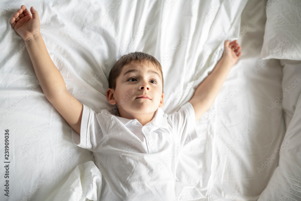 A Little boy lay on the bed with white blanket