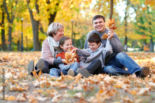 Happy family sit in autumn city park on fallen leaves. Children and parents posing, smiling, playing and having fun. Bright yellow trees.