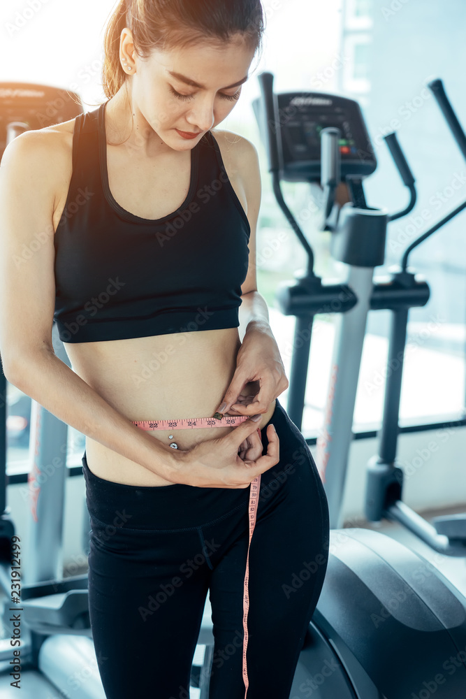 A young Asian woman wearing a workout in the fitness center are using waist measurement cables herself.