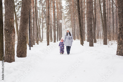 Winter, childhood and people concept - mother is walking with her little daughter in snowy forest