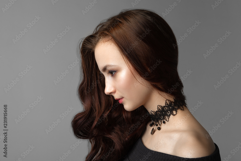 Pretty woman with long brown hairs on gray background.