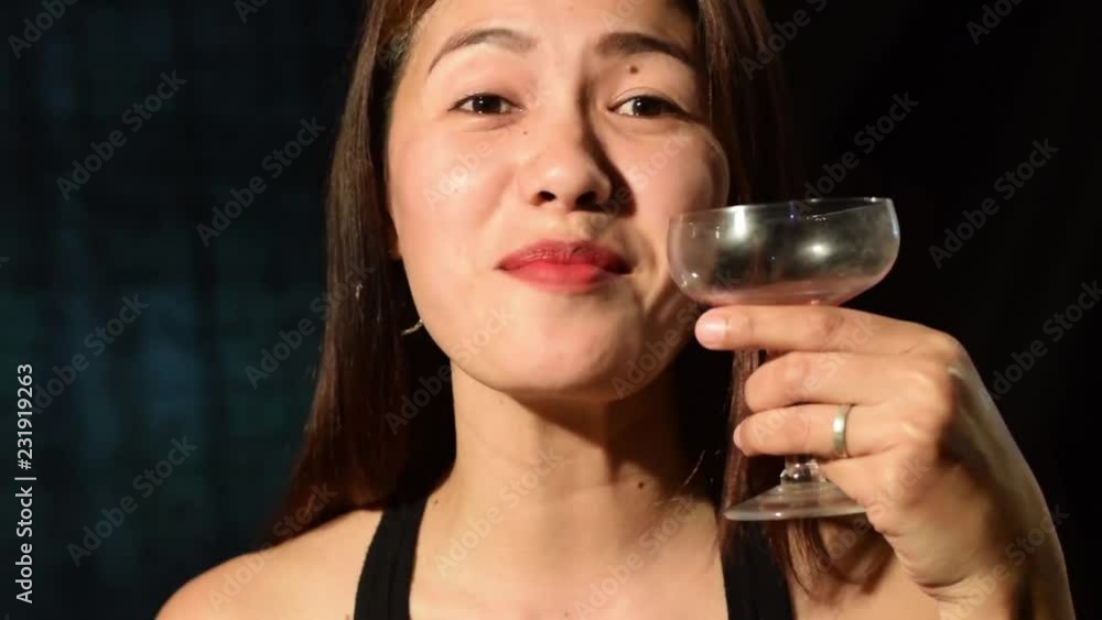 Beautiful Asian Hispanic middle age woman wearing black sleeveless drinking red wine on vintage glass. Dark Background, Close up Beautiful Asian Hispanic middle age woman wearing black sleeveless drinking red wine on vintage glass. Dark Background, Close up