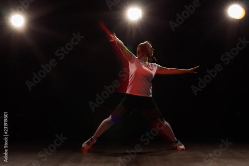 Dancing, sport, beautiful and people concept - young woman dancing in darkness jumped in colourful light