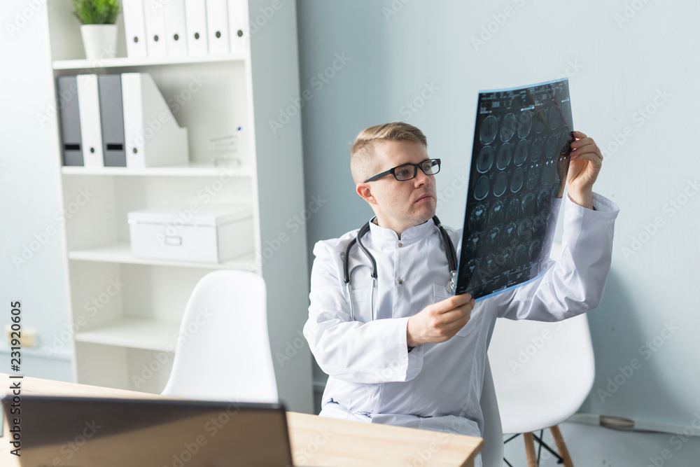 Medicine, healthcare and people concept - doctor examines an x-ray sitting behind a desk