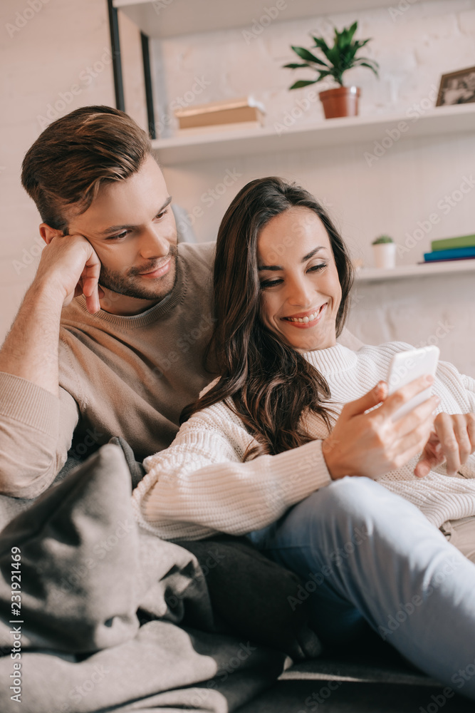 smiling young couple using smartphone together on couch at home smiling young couple using smartphone together on couch at home