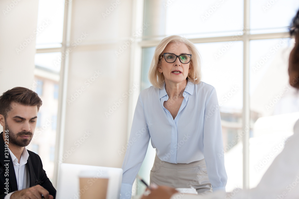 Serious mature businesswoman stand talk with employees at office meeting, middle female boss discuss project or strategy with workers at office briefing, confident woman negotiate with colleagues Stock Photo | Adobe