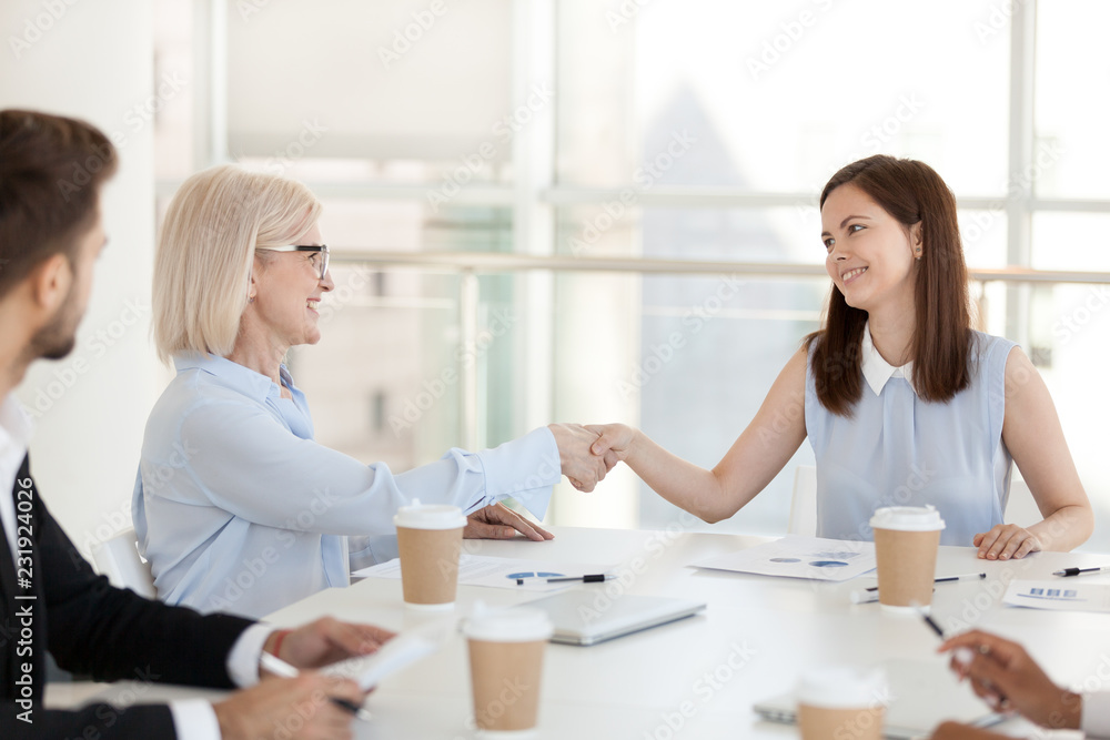 Happy millennial employee shake hand of mature colleague getting acquainted at meeting, diverse coworkers handshake greeting at briefing, introducing in boardroom or congratulating with promotion Happy millennial employee shake hand of mature colleague getting acquainted at meeting, diverse coworkers handshake greeting at briefing, introducing in boardroom or congratulating with promotion