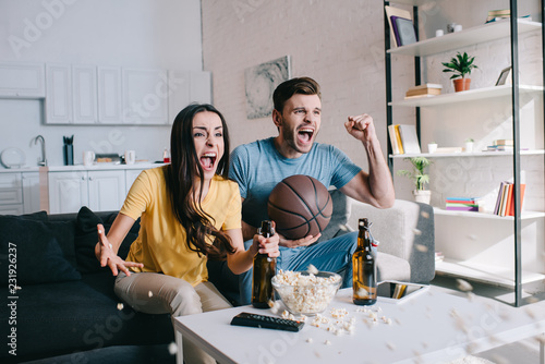 Bild auf Leinwand expressive young couple with beer cheering for basketball game at home