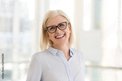 Portrait of smiling middle-aged businesswoman in glasses look in camera making headshot picture, happy mature female employee pose for picture in office, confident woman excited for new opportunities photo