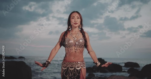 Beautiful tribal belly dancer outdoors. Woman in oriental costume dancing near the sea during sunset photo