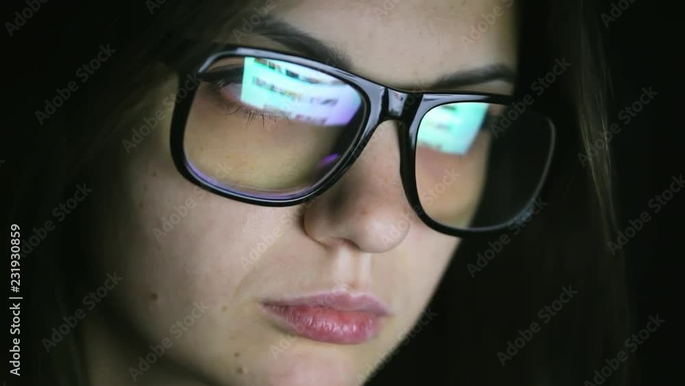 Attractive young woman working at night at computer at home, student girl browsing the internet, looking at monitor of modern computer, reflection on the glasses Attractive young woman working at night at computer at home, student girl browsing the internet, looking at monitor of modern computer, reflection on the glasses
