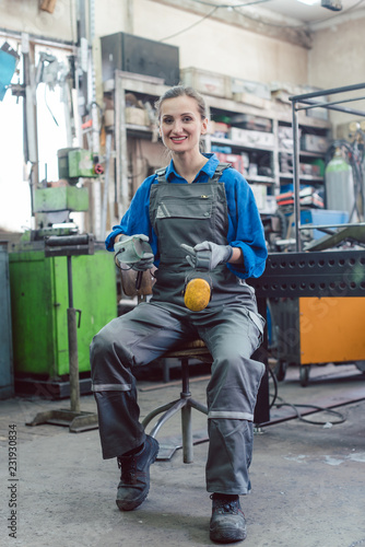 Female mechanic sitting in metal workshop looking and smiling into camera photo