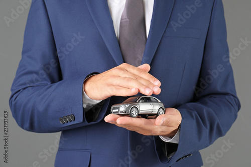 Insurance agent holding toy car on gray background, closeup