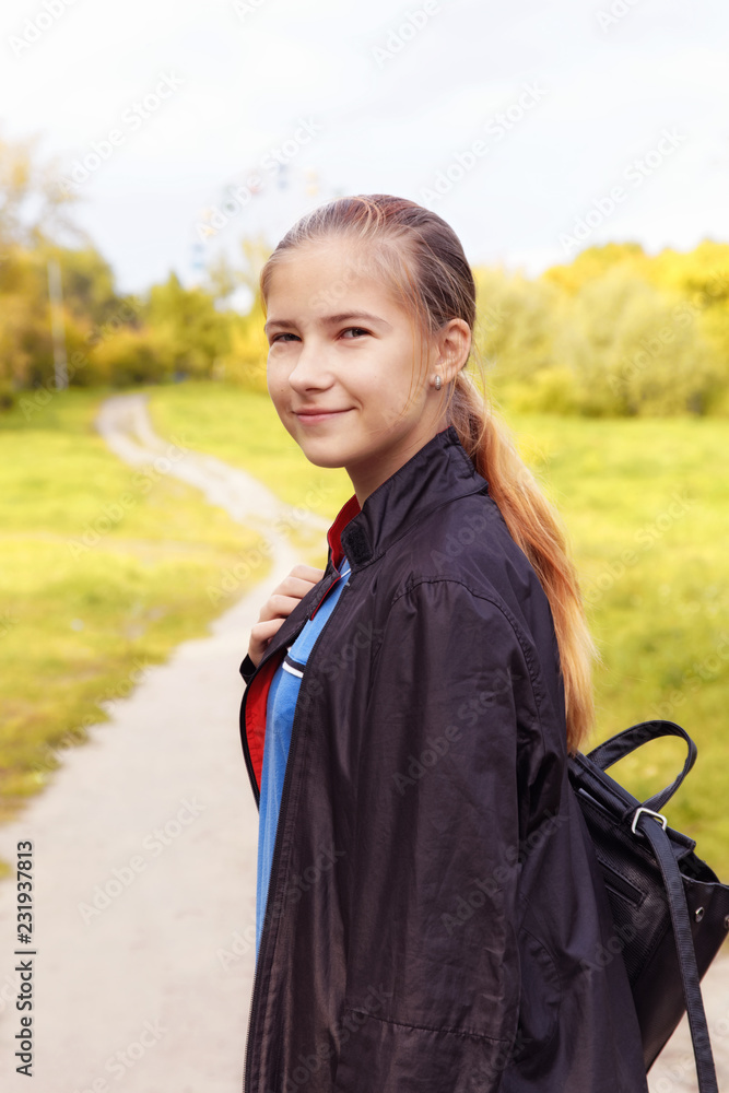 Cute teen girl with shoulder bag walking in the autumn park